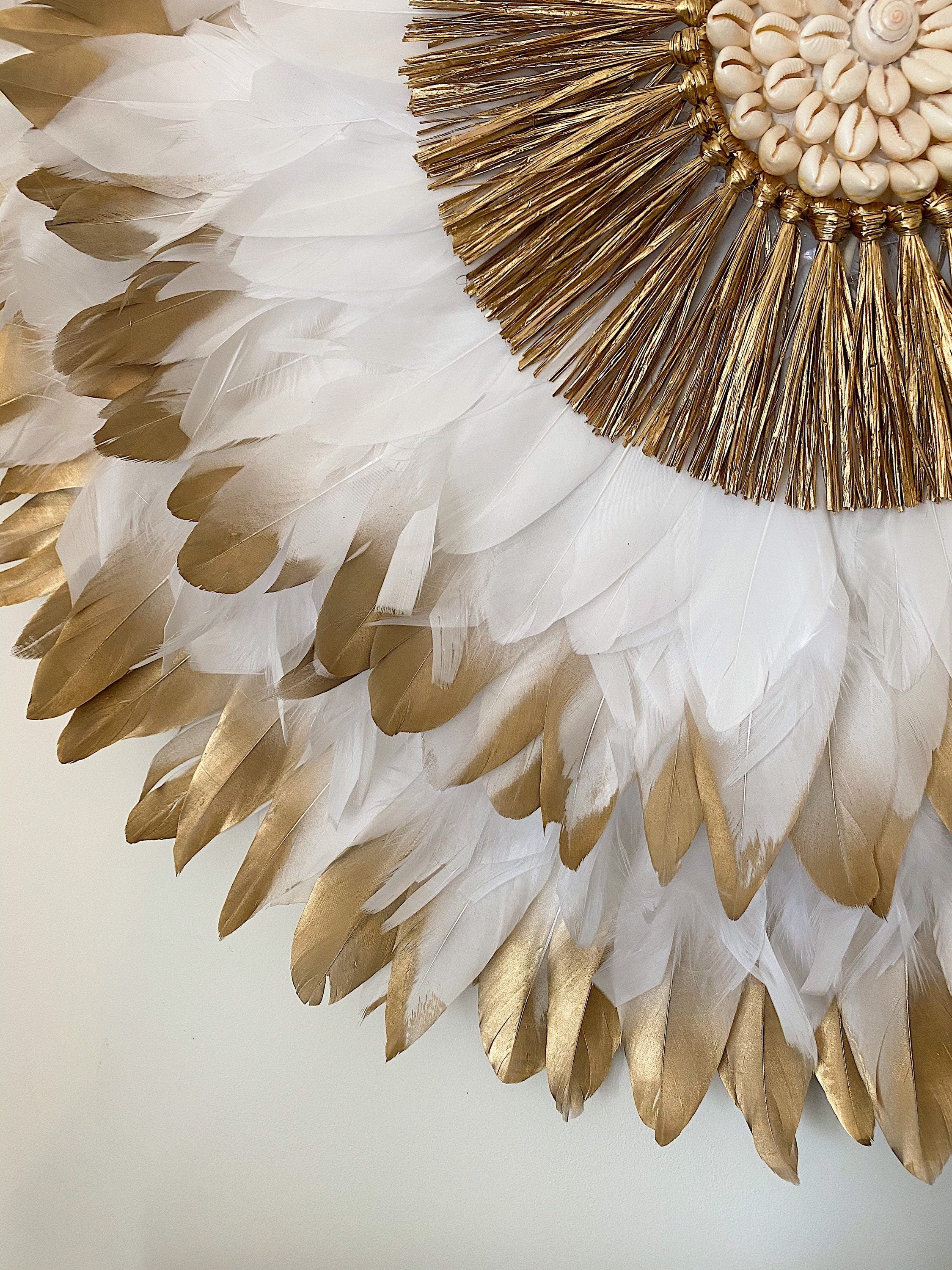 JUJUHAT « PRÉCIEUX DORÉ » avec ses plumes blanches et dorées et son cœur en raphia doré et coquillages cauris